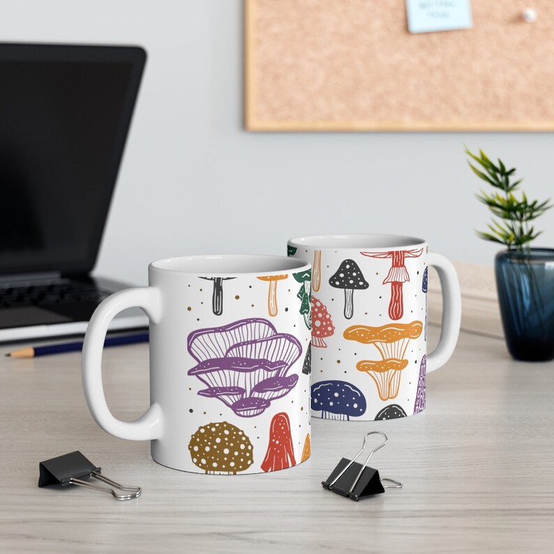 White ceramic mug featuring colorful illustrations of various mushrooms, perfect for mushroom enthusiasts and those who love nature-inspired designs.