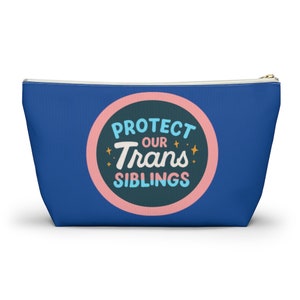 May include: A blue zippered pouch with a pink circle containing the text "Protect Our Trans Siblings" in a retro font with gold stars.