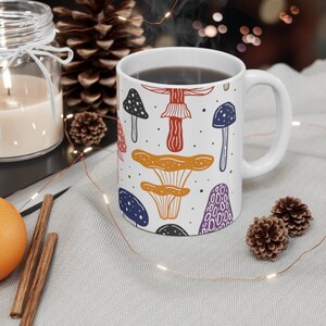 White ceramic mug featuring colorful illustrations of various mushrooms, perfect for mushroom enthusiasts and those who love nature-inspired designs.
