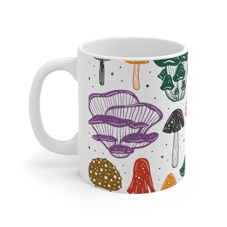 White ceramic mug featuring colorful illustrations of various mushrooms, perfect for mushroom enthusiasts and those who love nature-inspired designs.
