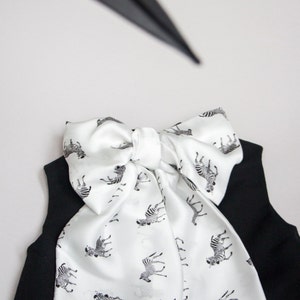 May include: A black sleeveless top with a white bow tie featuring a zebra print. The bow tie is tied in a knot at the neck.