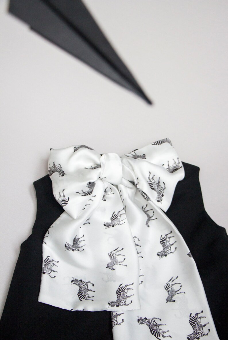May include: A black sleeveless top with a white bow tie featuring a zebra print. The bow tie is tied in a knot at the neck.