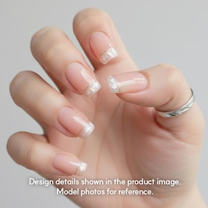 May include: Close-up of a hand with manicured nails. The nails are a natural pink with a white and iridescent glitter French tip. A silver ring is on the ring finger. The text at the bottom reads: Design details shown in the product image. Model photos for reference.