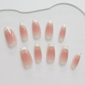 May include: A set of ten artificial nails with a light pink gradient design. Each nail has a glittery silver tip and a glossy finish. The nails are arranged on a white surface.