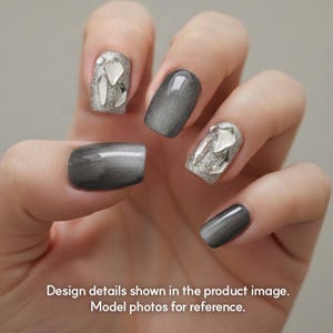 May include: Close-up of a hand with manicured nails. Some nails are a shimmering silver with large, clear gem accents. Other nails are a solid, glossy gray. The text at the bottom reads: Design details shown in the product image. Model photos for reference.