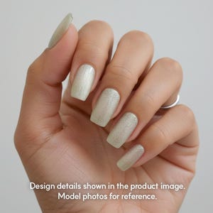 May include: Close-up of a hand with long, square-shaped nails painted in a shimmering, light green color. The nails have a glittery finish, reflecting light. The text at the bottom reads: Design details shown in the product image. Model photos for reference.