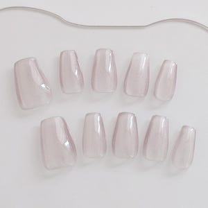 May include: A set of ten light purple press-on nails. The nails are rectangular with rounded edges and a glossy finish. They are arranged on a white surface, with a thin silver wire at the top.