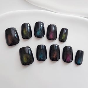May include: A set of ten black press-on nails with a glossy finish. Each nail features a shimmering, iridescent effect with hues of green, blue, and purple. The nails are arranged on a white surface.