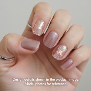 May include: Close-up of a hand with manicured nails in various shades of pink and nude. Some nails feature glitter accents. The text at the bottom reads "Design details shown in the product image. Model photos for reference."