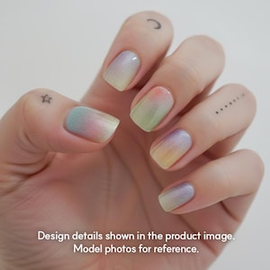 May include: Close-up of a hand with painted nails. The nails are painted with a gradient effect, transitioning from pastel colors like pink, green, yellow, and purple. The image also includes text that reads: Design details shown in the product image. Model photos for reference.