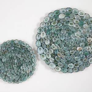 May include: Two circular wall decor pieces made of a mosaic of small, iridescent green seashells. The larger piece is about 12 inches in diameter, and the smaller piece is about 8 inches in diameter.