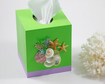 May include: A green tissue box cover with a purple trim and a seashell design. The design features seashells, coral, and starfish.