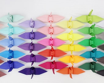 May include: A rainbow of origami paper cranes arranged in rows, with each row featuring a different color, from light pink to dark gray.