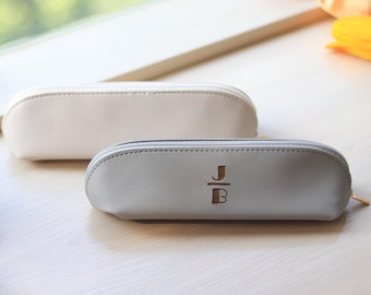 May include: Two zippered pencil cases, one white and one gray. The gray case has the initials "J/B" embossed on the front.