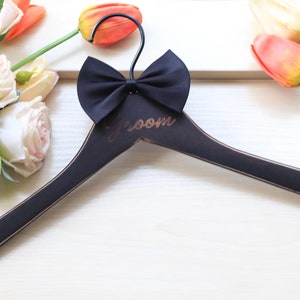 May include: Black wooden hanger with a black bow tie and the word "Groom" engraved in gold lettering.
