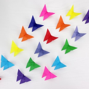 May include: A collection of 17 origami butterflies in a rainbow of colours, including red, orange, yellow, green, blue, purple, and pink. The butterflies are arranged in a loose pattern on a white surface.