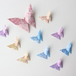 May include: A collection of ten origami butterflies in various pastel colors, including pink, blue, and yellow, with floral patterns. The butterflies are arranged on a white background.