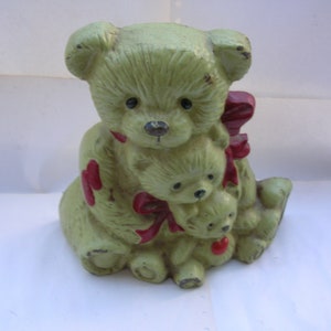 May include: A green ceramic doorstop shaped like a mother bear and two cubs. The bears are all wearing red bows.