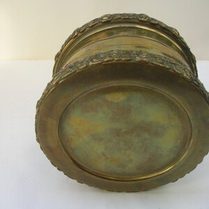 May include: A round, brass planter with a decorative, floral design around the rim. The planter has a smooth, brass bottom.