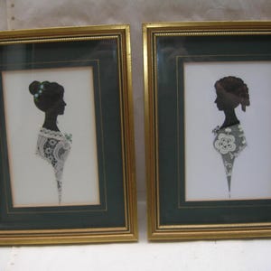 Può includere: Due ritratti di silhouette incorniciate di donne. Le silhouette nere sono ambientate su uno sfondo bianco, con cornici dorate e passe-partout verde scuro. Le donne indossano pizzi e dettagli floreali. Le cornici sono rettangolari.