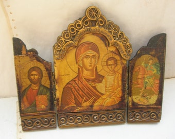 May include: A wooden triptych icon with three panels. The center panel depicts the Virgin Mary holding the baby Jesus. The left panel shows a portrait of Jesus, and the right panel shows a saint on horseback. The icon is painted in gold, red, and blue.