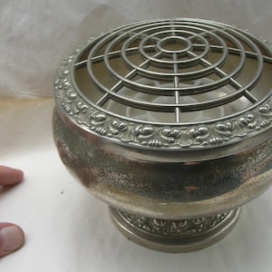 May include: Silver flower frog with a decorative floral design around the rim and a wire mesh top. The frog has a round base.