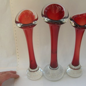Könnte beinhalten: Set aus drei roten Glasvasen mit klaren Glasböden. Die Böden haben ein strukturiertes, blasenartiges Design.