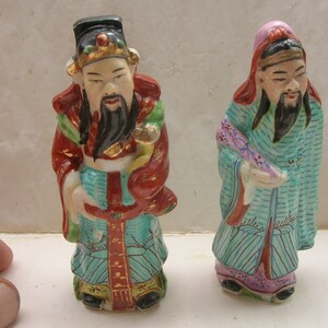 Peut inclure: Deux figurines en porcelaine de dieux chinois, l'une en robes rouges et bleues avec une couronne dorée, l'autre en robes bleues et roses avec un chapeau rose.
