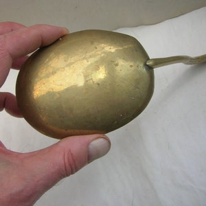 May include: A brass spoon with a rounded bowl and a long, curved handle. The spoon is tarnished and has a worn finish.