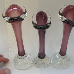 Könnte beinhalten: Set aus drei violetten Glas-Blumenvasen mit klaren Glasböden. Die Böden haben ein strukturiertes Blasendesign.