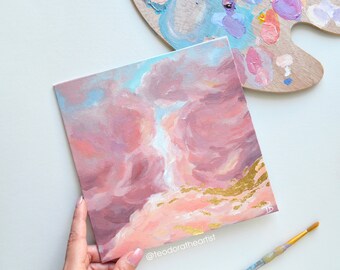 Könnte beinhalten: Ein kleines Gemälde, das einen rosa und blauen Himmel mit goldenen Akzenten zeigt. Das Gemälde ist auf Leinwand und wird von einer Hand gehalten. Das Gemälde ist mit dem Buchstaben "B" signiert.