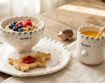 Children's white ceramic Stegosaurus-shaped dinnerware set consisting of a dinner plate, bowl, and cup. Decorated in green.