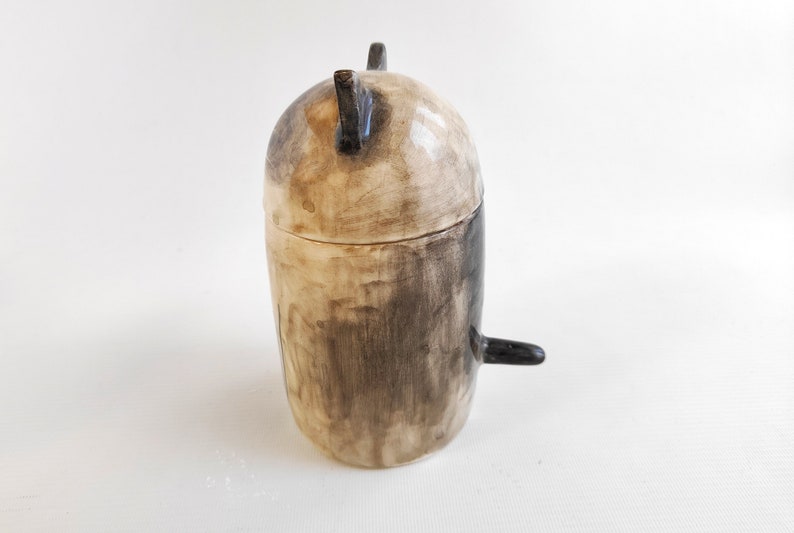 May include: A ceramic jar with a lid, painted in black and white. The jar has a rounded shape and a small handle on the side.