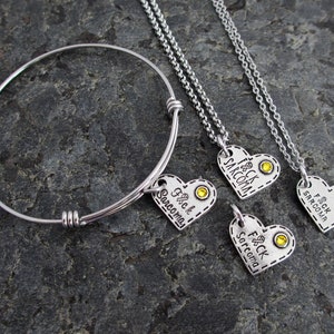 May include: Three silver necklaces with heart-shaped pendants. Each pendant has the text "F*ck Sarcoma" and a yellow rhinestone. One necklace is a bracelet.