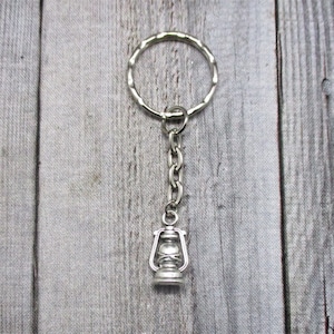 May include: A silver keychain with a small, detailed lantern charm. The keychain is attached to a silver key ring.