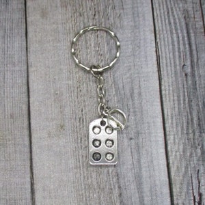 May include: Silver keychain with a rectangular charm featuring a grid of nine circles. The keychain is attached to a silver ring.