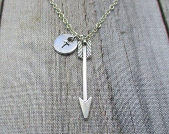 May include: A silver necklace with a small silver circle charm with the letter "T" on it and a silver arrow charm hanging from it.