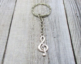 May include: Silver treble clef keychain with a silver ring and chain. The keychain is on a wooden background.
