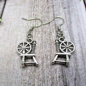 May include: Silver spinning wheel earrings with a detailed design. The earrings are on a wooden surface.