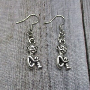 May include: A pair of silver dangle earrings featuring a small, detailed figurine of a sitting goblin or elf.