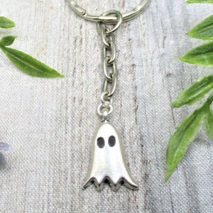 May include: A silver ghost keychain with a silver key ring and chain. The ghost has two black eyes.