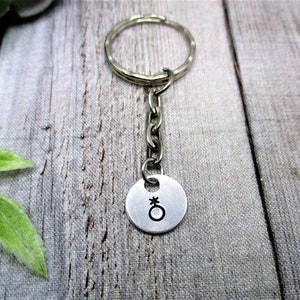 May include: Silver keychain with a round charm featuring a gender neutral symbol.