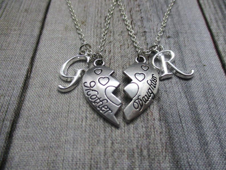 May include: Two silver necklaces with matching heart pendants that say "Mother" and "Daughter". Each pendant has a small heart charm and a letter charm, "G" and "R".