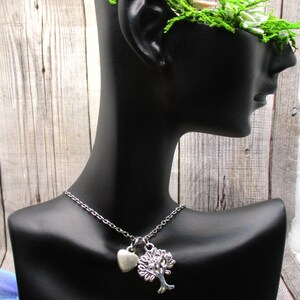 Puede incluir: Un collar de plata con un dije de &aacute;rbol y coraz&oacute;n. El collar est&aacute; en un busto de maniqu&iacute; negro.