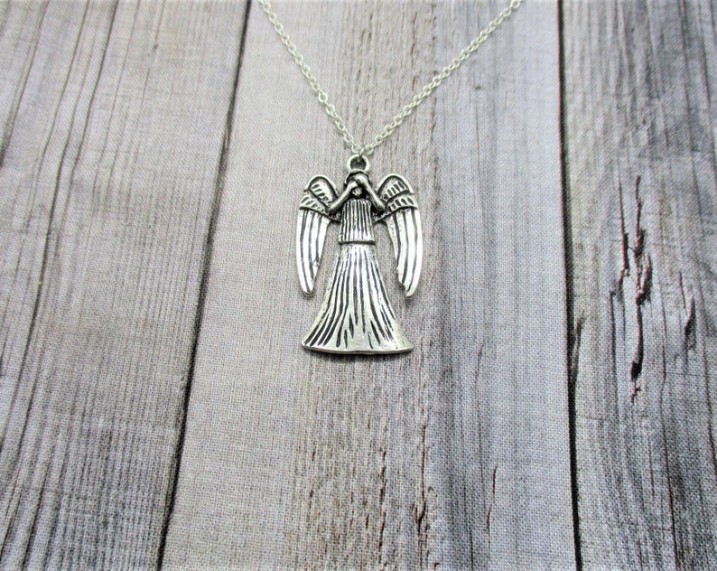 May include: Silver necklace with a Weeping Angel pendant. The angel is depicted with its wings outstretched and its head bowed.