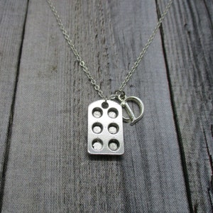 May include: Silver necklace with a charm that looks like a muffin tin. The charm has eight round indentations. The necklace has a silver clasp.