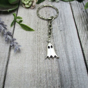 May include: A silver ghost keychain with a key ring. The ghost has two small eyes and a jagged bottom.