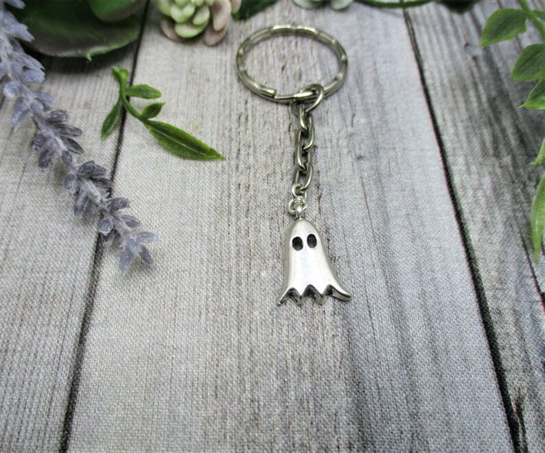May include: A silver ghost keychain with a key ring. The ghost has two small eyes and a jagged bottom.