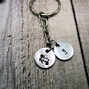 May include: Silver keychain with a round charm featuring an image of a ram and a second round charm with the letter "M" engraved on it.