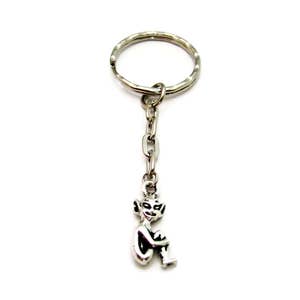 May include: A silver keychain with a small, detailed figurine of a sitting goblin. The goblin has large ears and is holding its hands together.